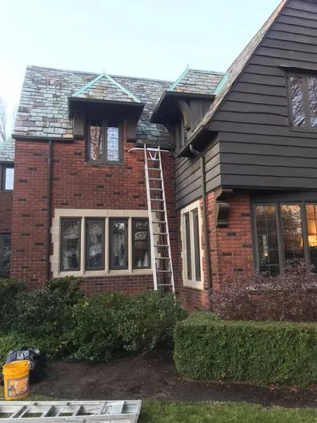 G&L ladder set against a brick and shingle-sided home with tall windows